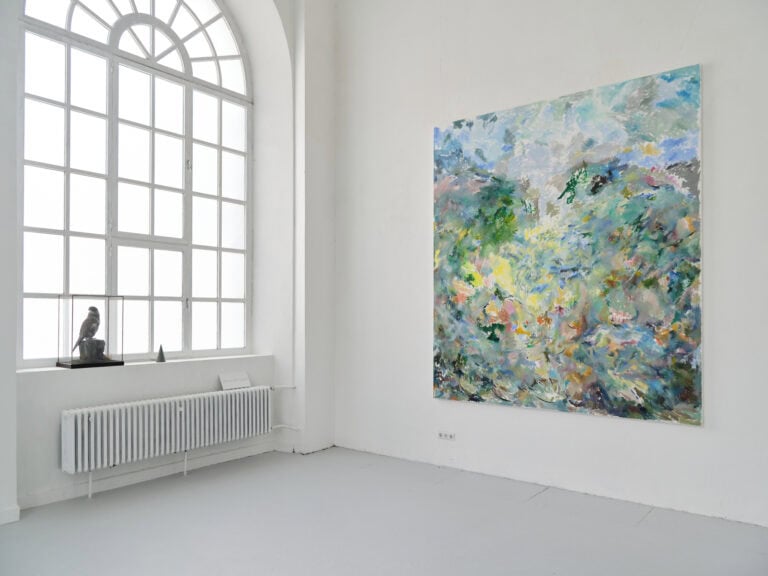 Foto: Ansicht eines Raumes mit weißen Wänden, grauem Boden und einem großen Bogenfenster. An der Wand hängt ein großformatiges, buntes Gemälde. Auf der Fensterbank stehen zwei Objekte.
