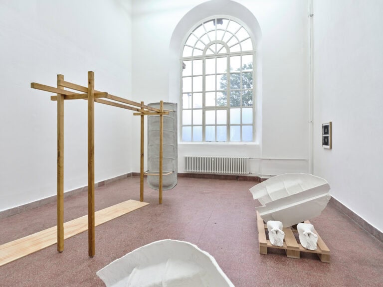 Foto: Ansicht eines Raumes mit weißen Wänden, rötlichem, gekachelten Boden und einem großen Bodenfenster. Im Raum befinden sich einige große Skulpturen, an der Wand befindet sich ein Objekt.
