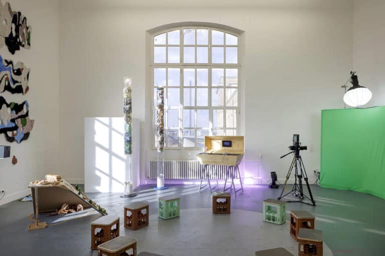 Foto: Ansicht eines Raumes mit weißen Wänden, grauem Boden und einem großen Bogenfenster. Auf dem Boden und an den Wänden des Raumes verteilt eine Vielzahl von Objekten.