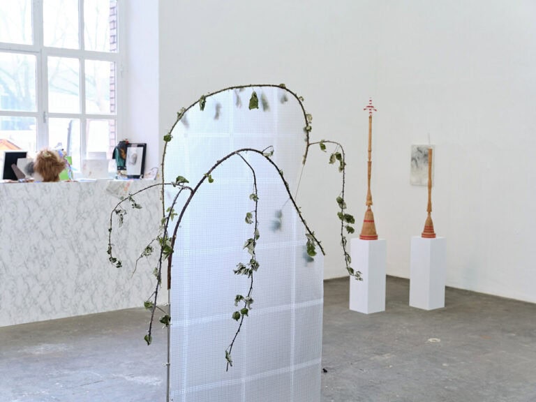 Foto: Ansicht eines Raumes mit weißen Wänden, grauem, steinernen Boden und einem Fenster. Im Raum, an den Wänden und auf der Fensterbank befinden sich Objekte. Die Wand unter dem Fenster ist mit einer gräulich-weißen Musterung versehen.