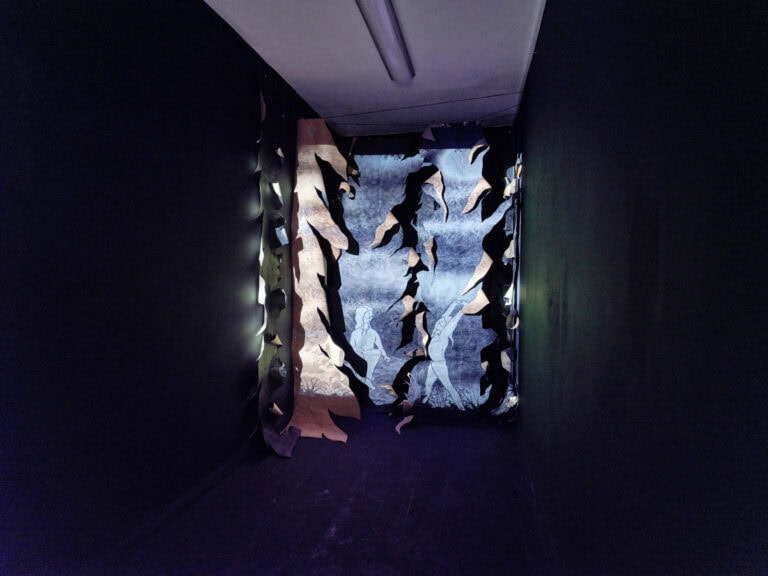 Foto: Ansicht eines abgedunkelten Raumes mit weißer Decke. Im Raum befindet sich eine Konstruktion aus unterschiedlichen Materialien.