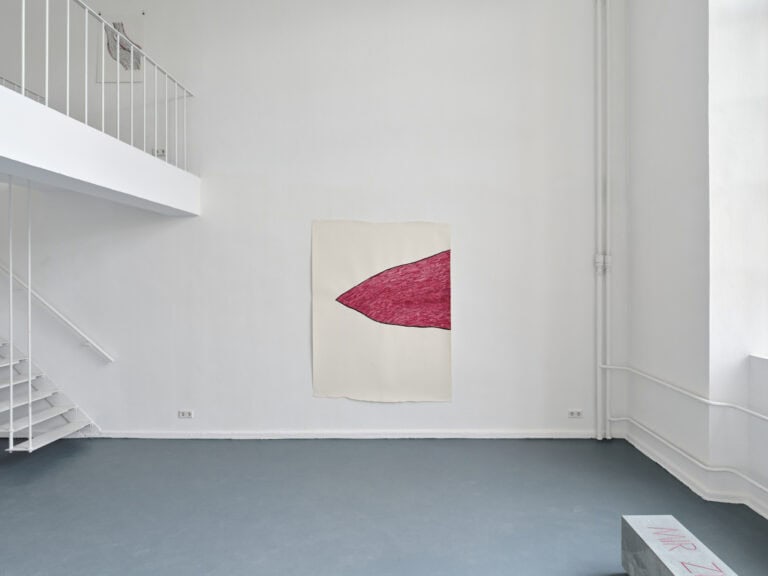 Foto: Ansicht eines Raumes mit weißen Wänden, grauem Boden und einer zweiten, durch eine Treppe begehbaren Ebene. An der Wand hängt eine großformatige Papierarbeit.