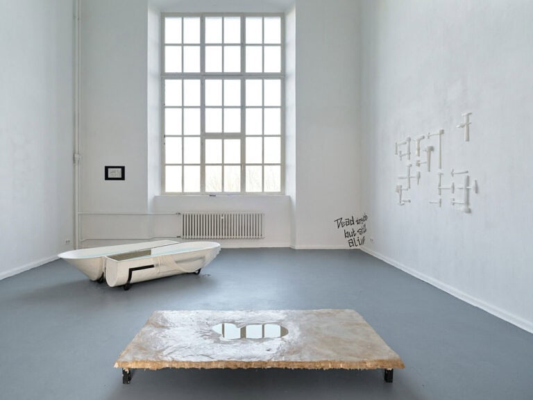 Foto: Ansicht eines Raumes mit weißen Wänden, grauem Boden und einem großen Bogenfenster. An den Wänden und auf dem Boden des Raumes befinden sich unterschiedliche Objekte.