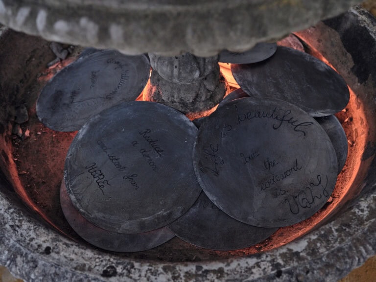 Foto: Nahaufnahme von runden, schwarzen Platten in einem steinernen Behältnis. Die Platten sind mit Schrift versehen. Lesbar sind die Sätze: "Life is beautiful but the Codeword is UGLY" und " Reduce a demon and start from HERE". Hinter den platten scheint ein rötliches Licht.