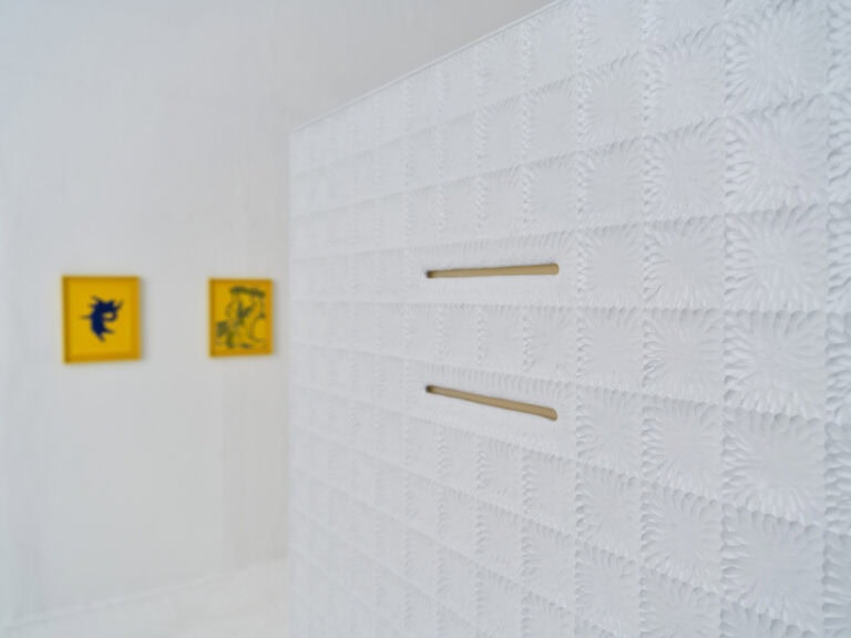 Foto: Nahaufnahme eines Objektes mit weißer, gleichmäßig gemusterter Oberfläche. Im Hintergrund sind weitere Objekte an der Wand zu erkennen.