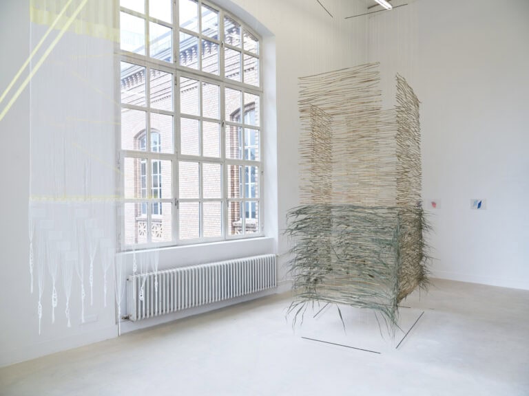 Foto: Ansicht eines Raumes mit weißen Wänden, grauem Boden und einem großen Bogenfenster. Im Raum befinden sich zwei Objekte, durch die man hindurchsehen kann. An den Wänden befinden sich weitere kleinformatige, flache Objekte.