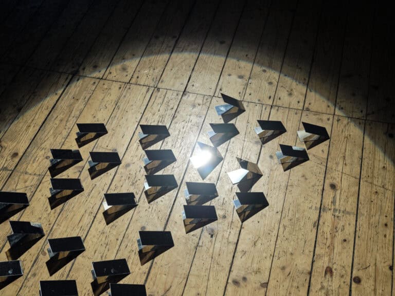 Foto: Nahaufnahme einer Gruppe von Objekten auf Dielenboden. Die Objekte werden von Licht angestrahlt und reflektieren dieses zum Teil.
