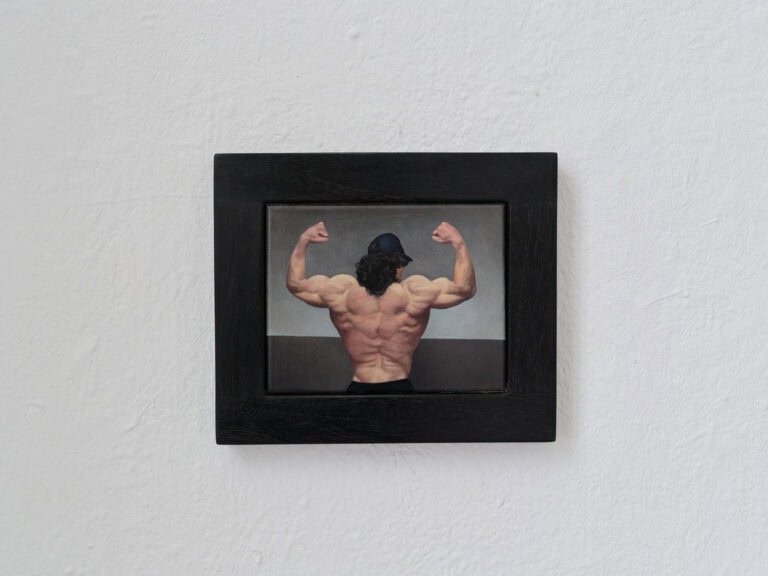 Foto: Nahaufnahme einer gerahmten Arbeit vor einer weißen Wand.