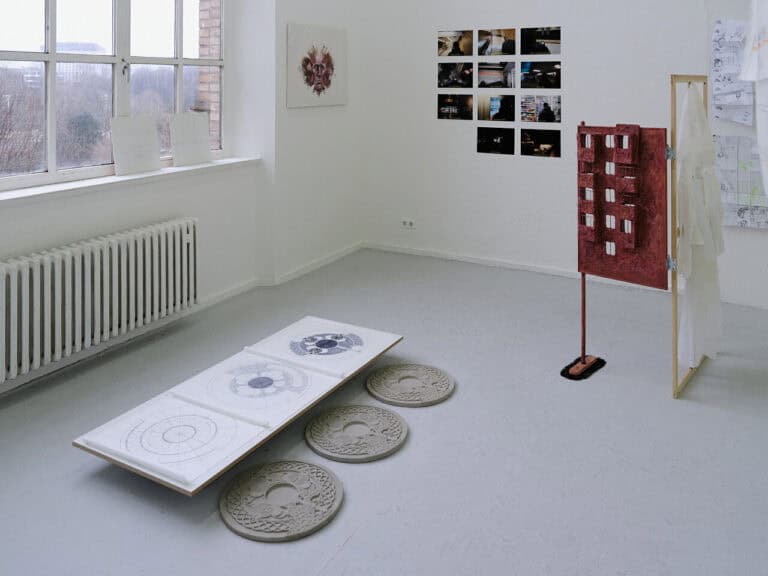 Foto: Ansicht eines Raume mit grauem Boden, weißen Wänden und Fenster. Auf dem Boden, auf der Fensterbank und an den Wänden befinden sich Objekte.