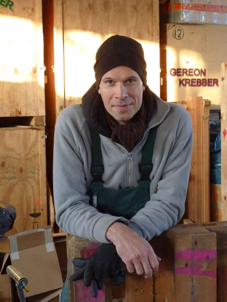 Foto: Porträt eines nach vorne gelehnten Mannes in einem Raum mit hölzernen Boxen. Im Hintergrund der Schriftzug "Gereon Krebber".