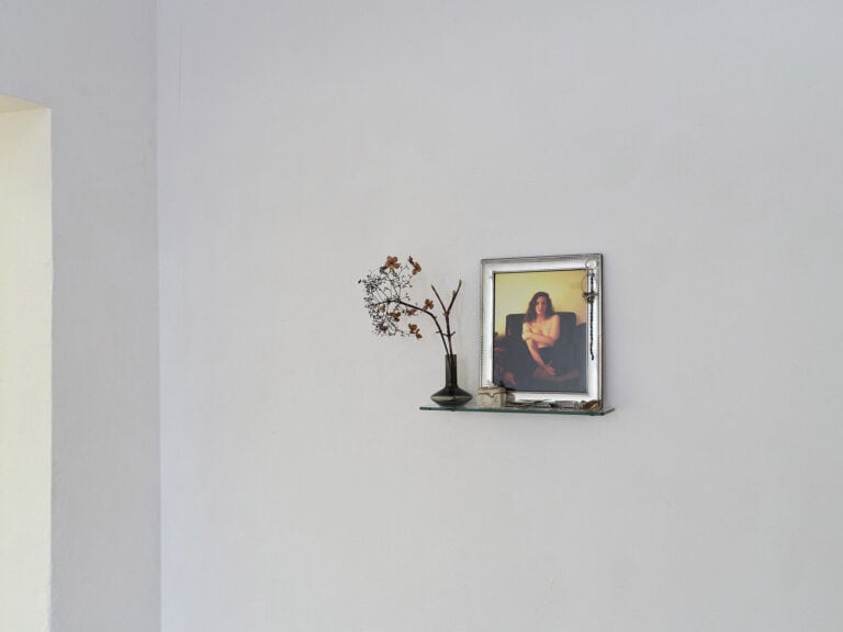 Foto: Ansicht eines Raumecke mit weißen Wänden. An der Wand ein Objekt, bestehend aus unterschiedlichen Materialien.